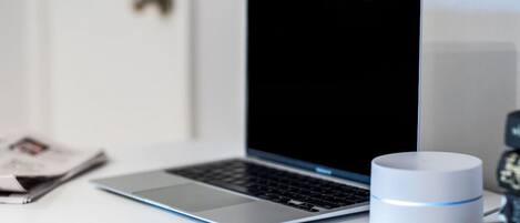 A laptop on a white desk with a white cylindrical object beside it.