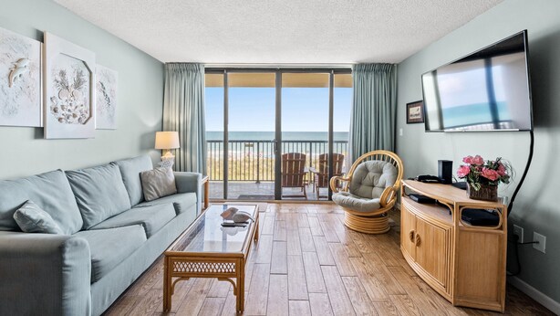Un salon avec un canapé, une table basse et un téléviseur. Il y a un balcon avec vue sur l’océan.
