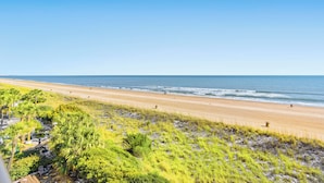 Ein Strand mit freiem Blick auf den Ozean, sandigem Ufer und etwas Grün im Vordergrund.