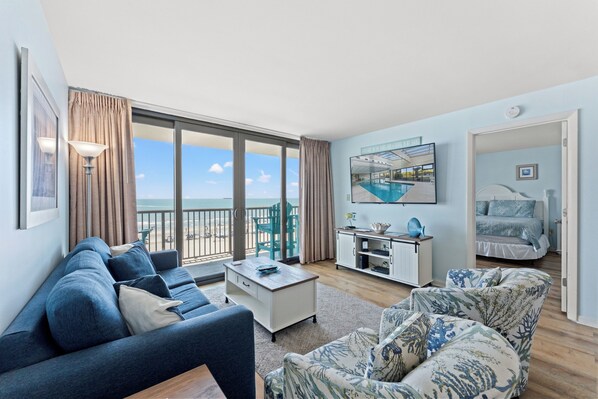 A living room with a sofa, a coffee table, and a view of the beach.