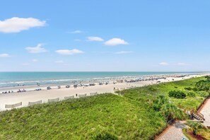 A beach with a long stretch of sand, a wooden fence, and a grassy area with a pathway.