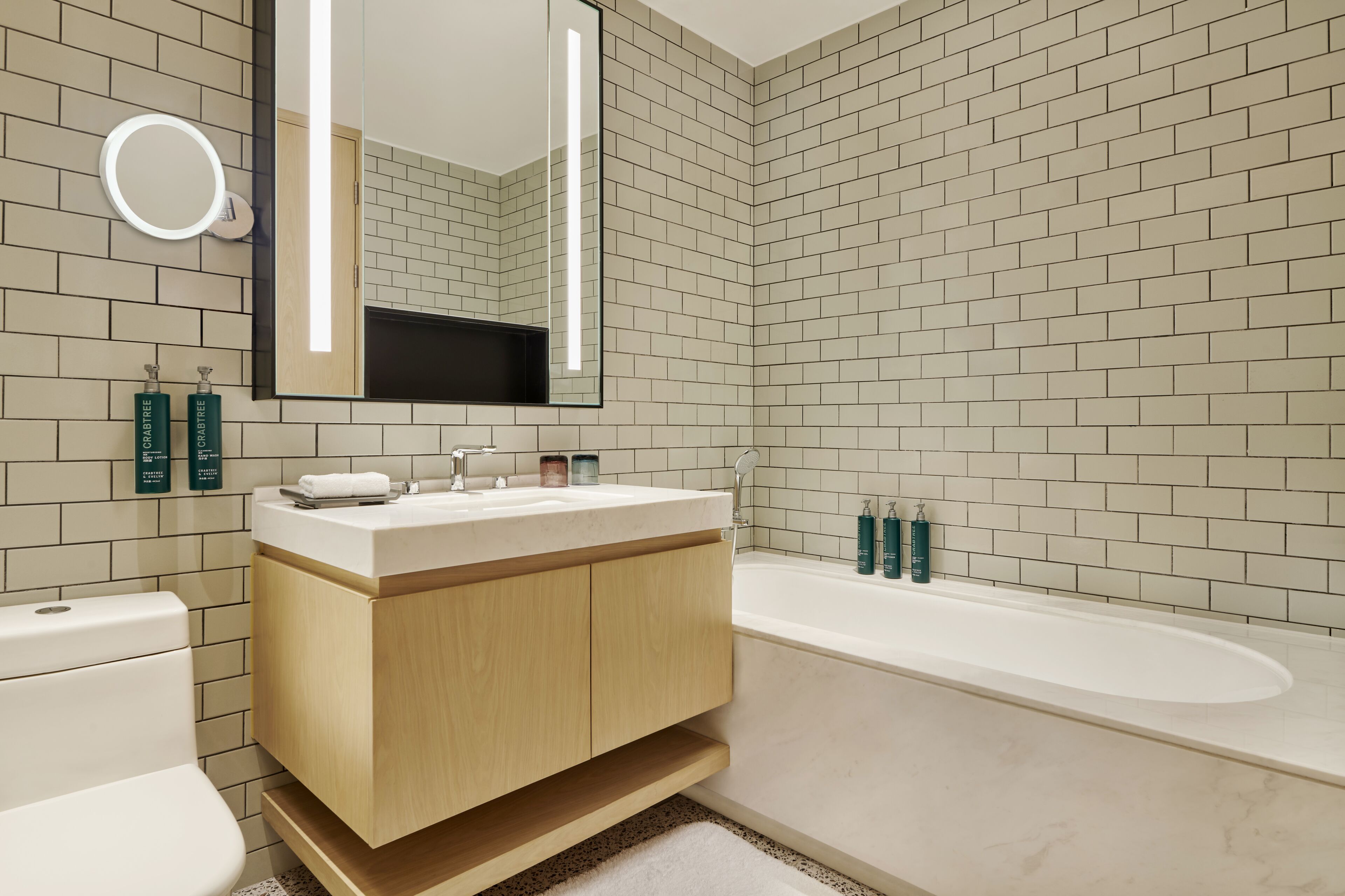A modern bathroom with a white toilet, wooden vanity, a large mirror, and a bathtub.