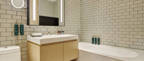 Un baño moderno con inodoro blanco, tocador de madera, un espejo grande y una bañera.