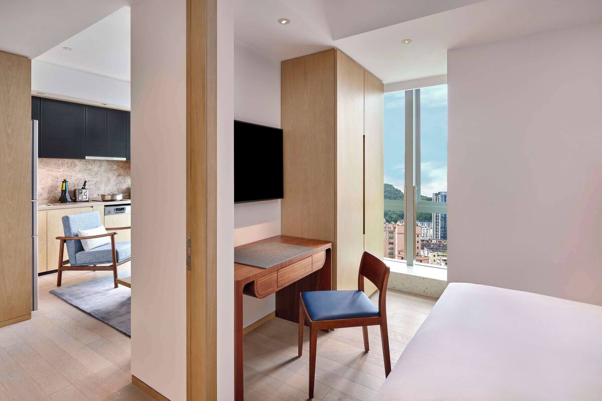 Une chambre d’hôtel moderne avec un bureau en bois, une chaise, un lit et une grande fenêtre donnant sur la ville.