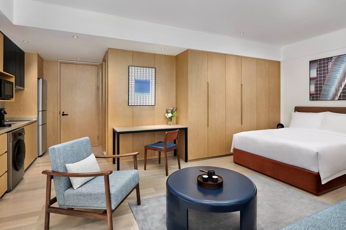 Une chambre d’hôtel de taille réduite, comprenant un lit, un bureau, une chaise, une petite table et un lave-linge.