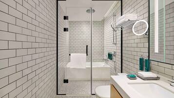 Un baño moderno con azulejos tipo metro blancos, una ducha con cerramiento de vidrio, una bañera blanca y un espejo grande.