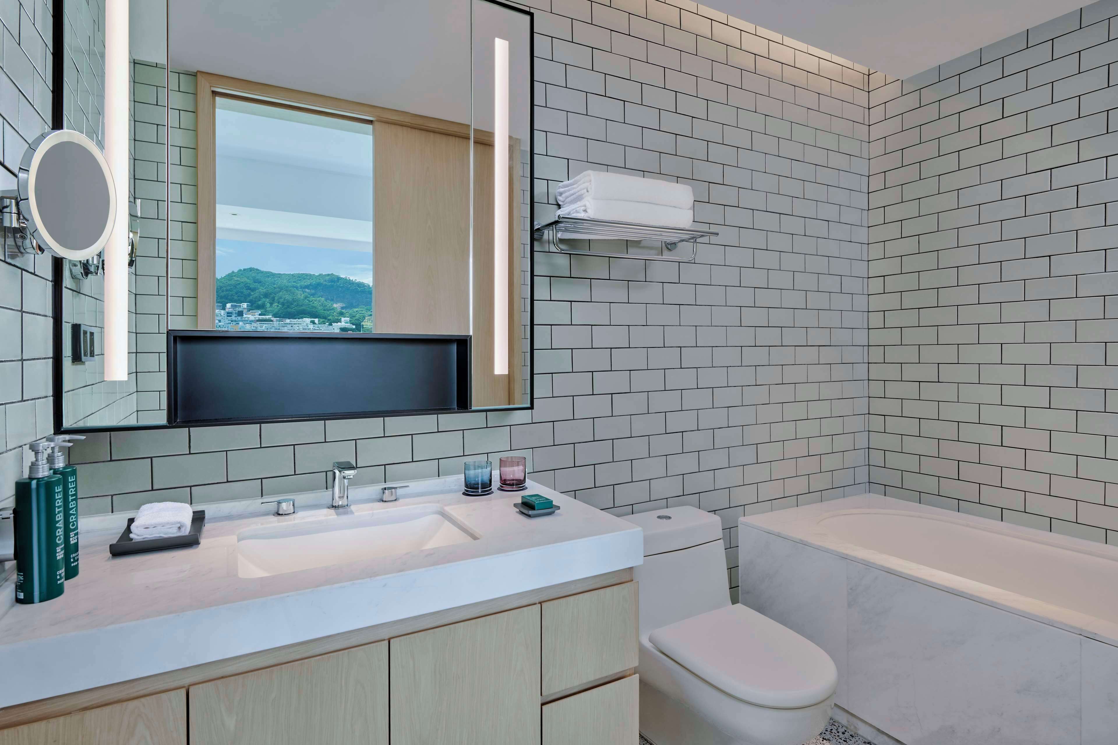 A modern bathroom with a large mirror, a sink with toiletries, a toilet, and a bathtub.