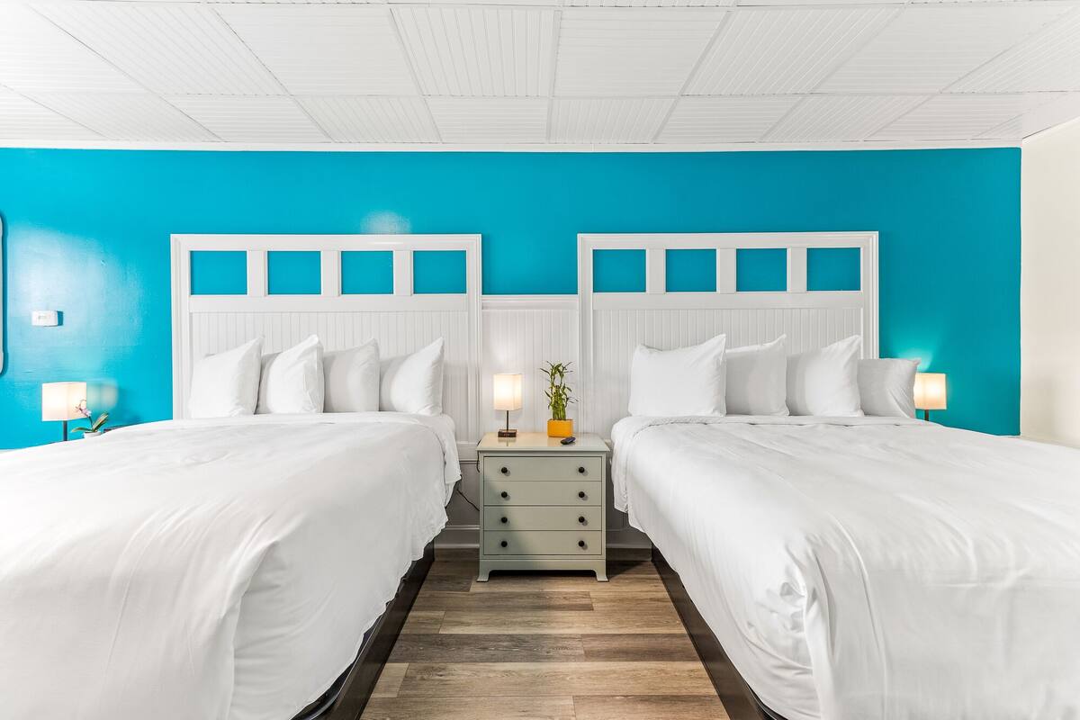 A hotel room with two beds, a nightstand, and a wall painted in bright blue.