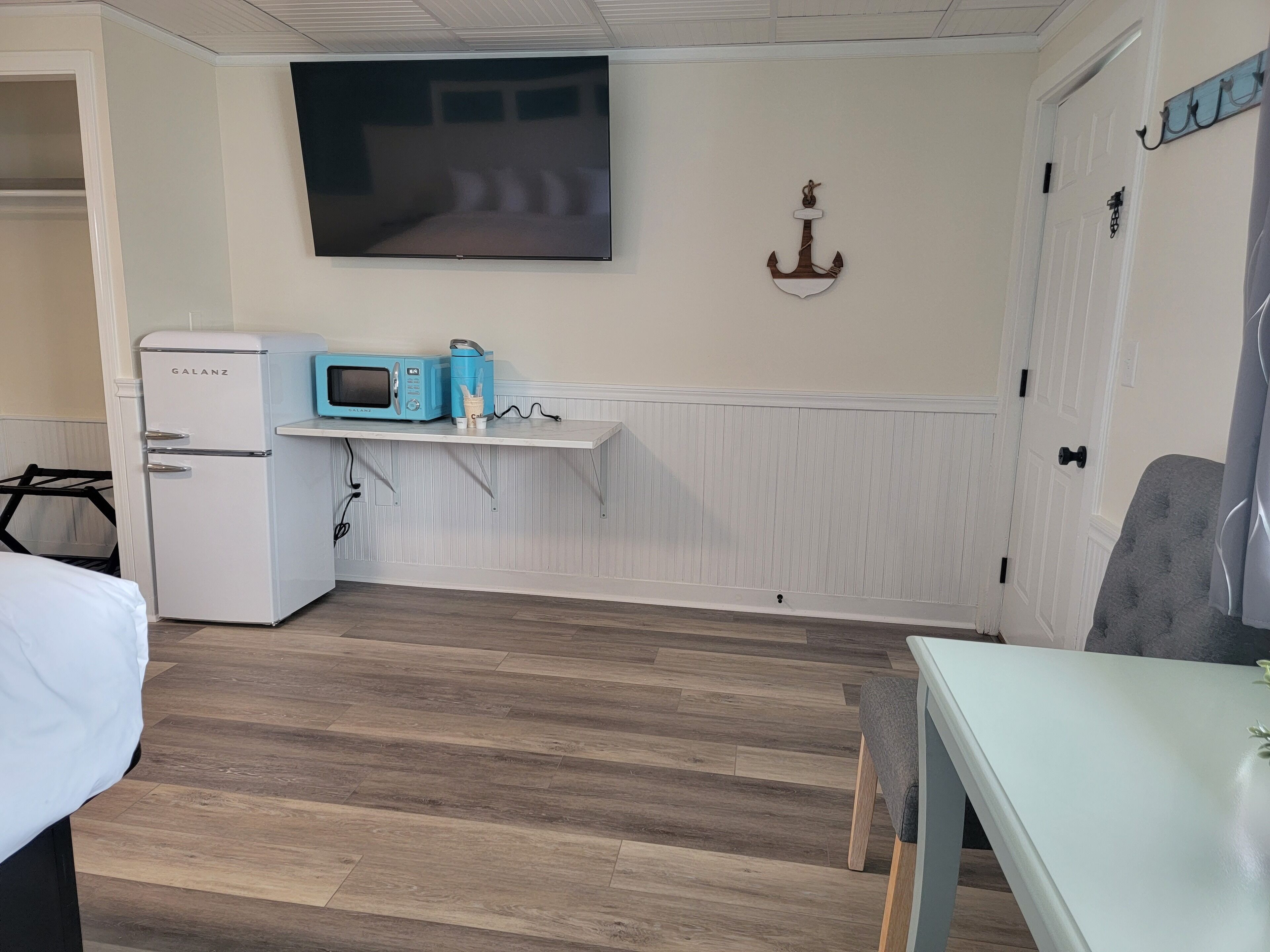 Une pièce avec un réfrigérateur blanc, un four à micro-ondes, une petite table et un téléviseur fixé au mur.