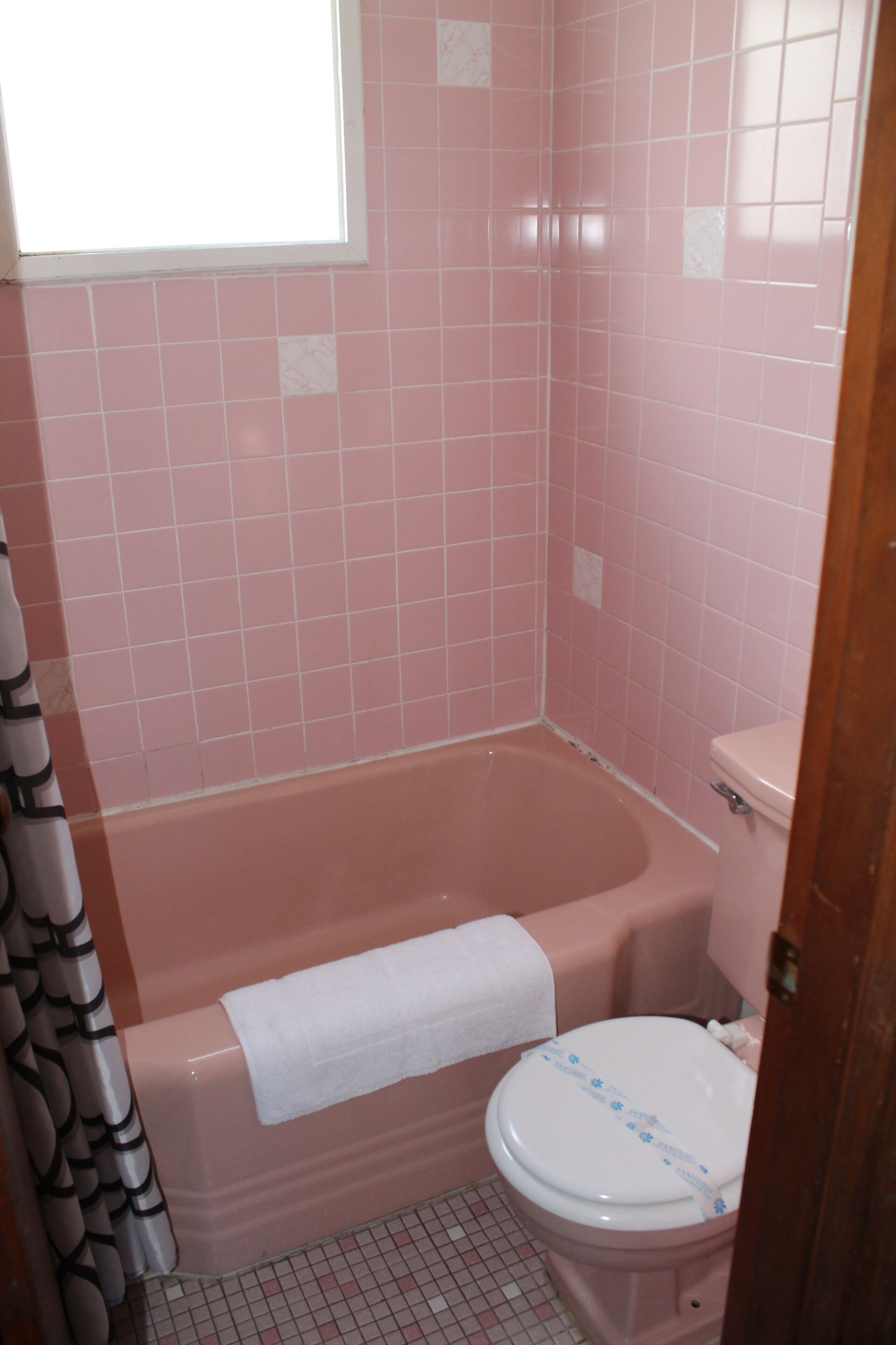 A bathroom with pink tiles, a white bathtub, and a toilet.