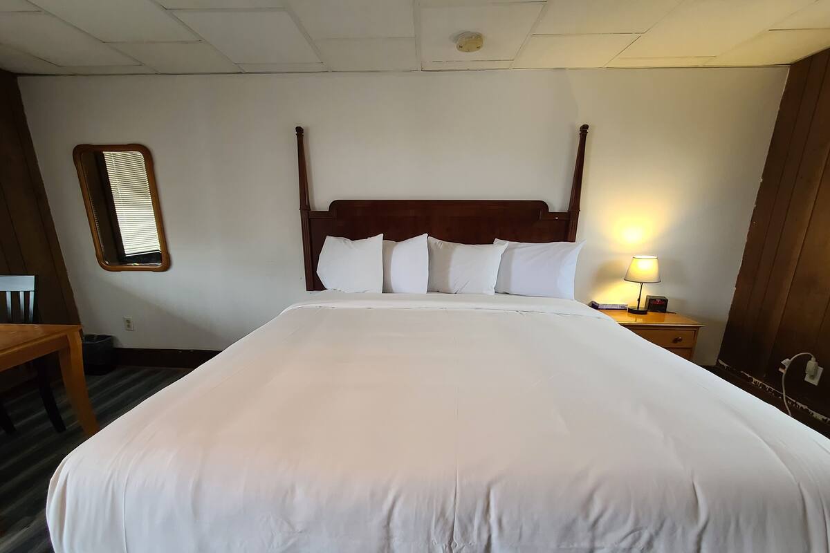 A large bed with white linens, a wooden headboard, and a bedside lamp.
