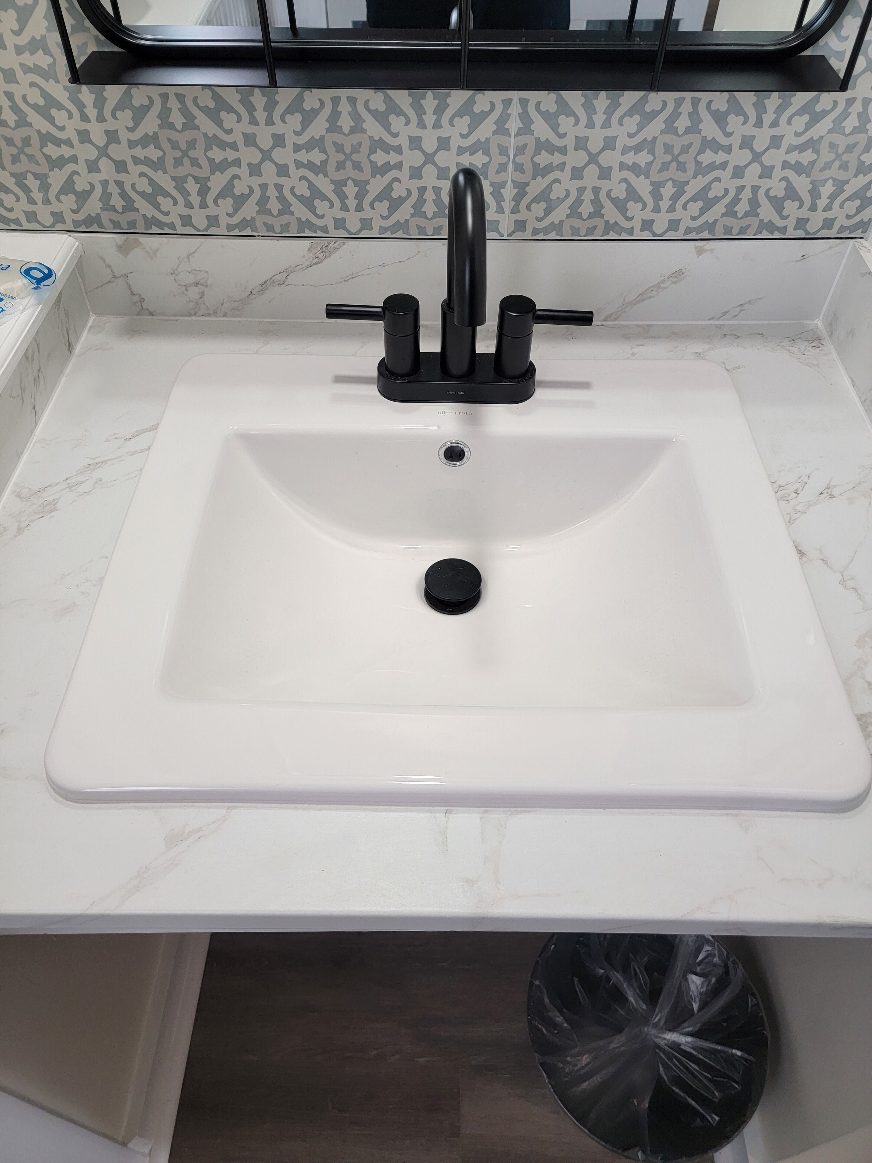 Un lavamanos de baño con un grifo moderno, una encimera de mármol y un cubo de basura.