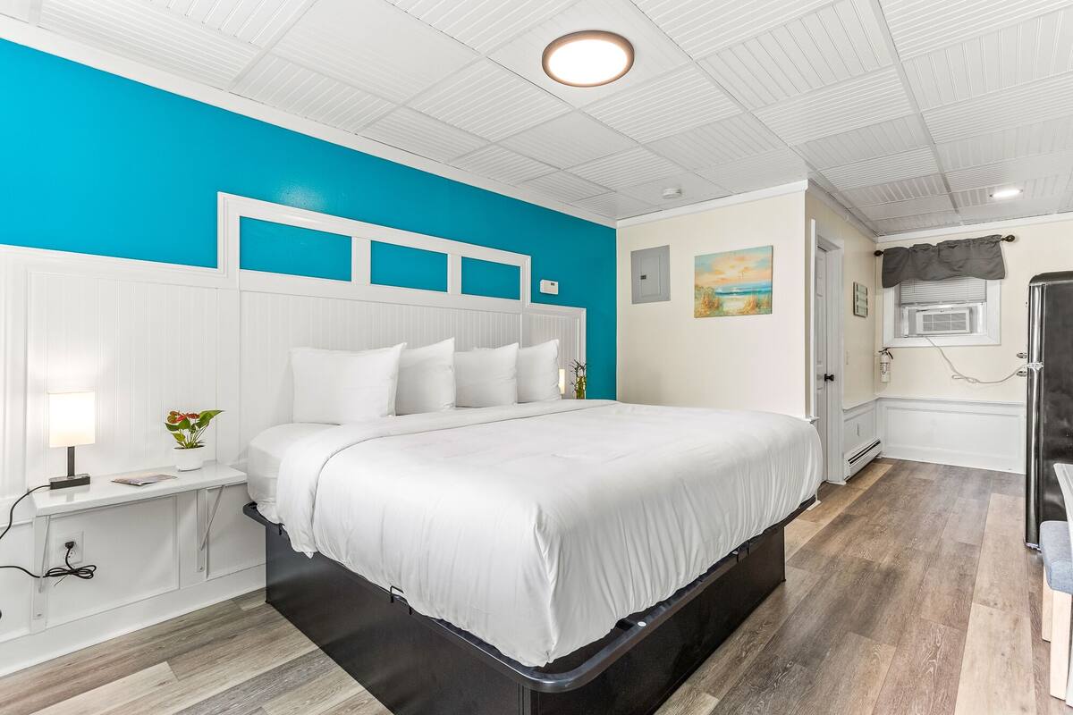 A modern bedroom with a white bed, teal accent walls, and a wooden floor.