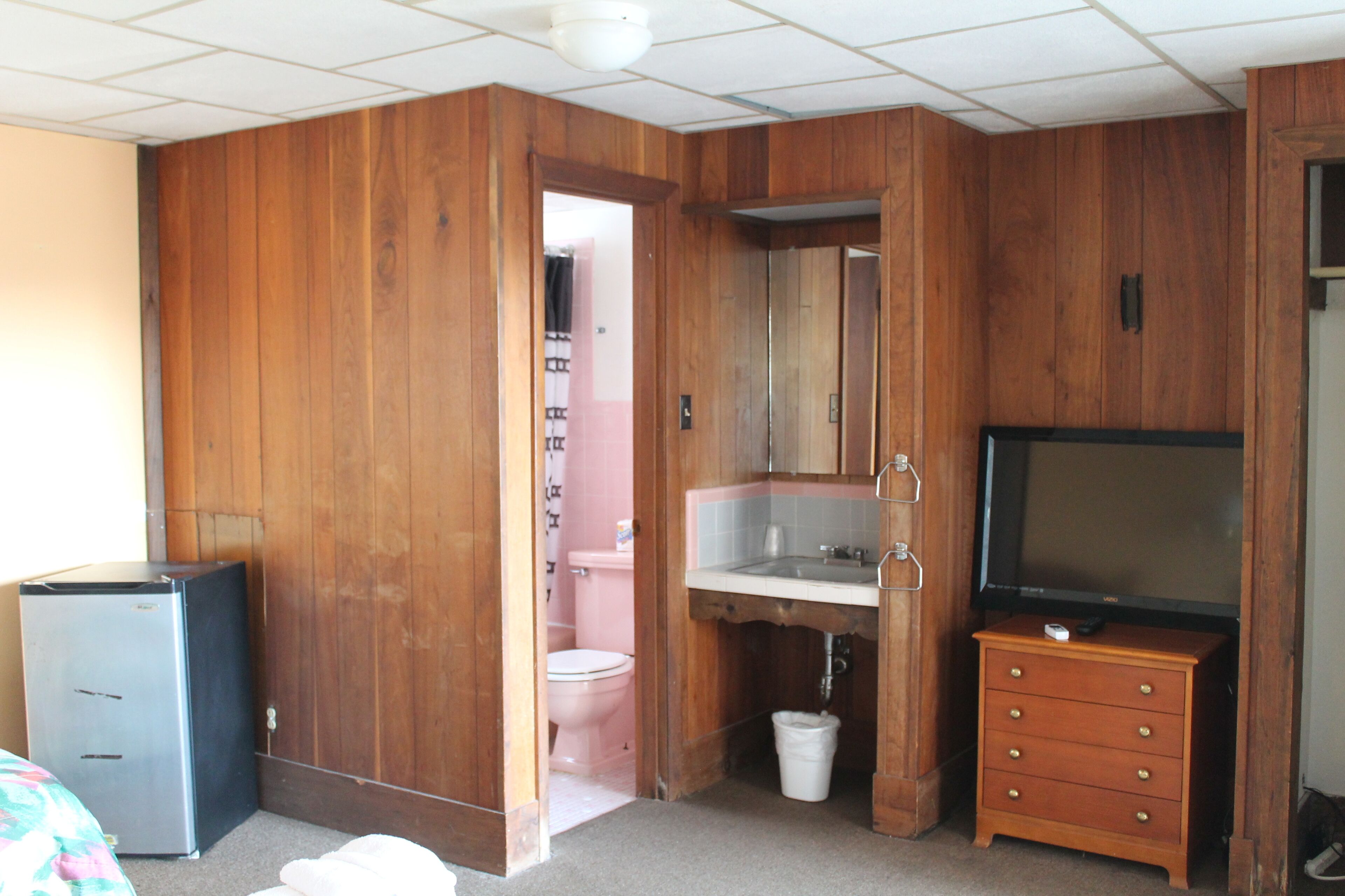 A compact room with a wooden wardrobe, a small sink, a television, and a refrigerator.