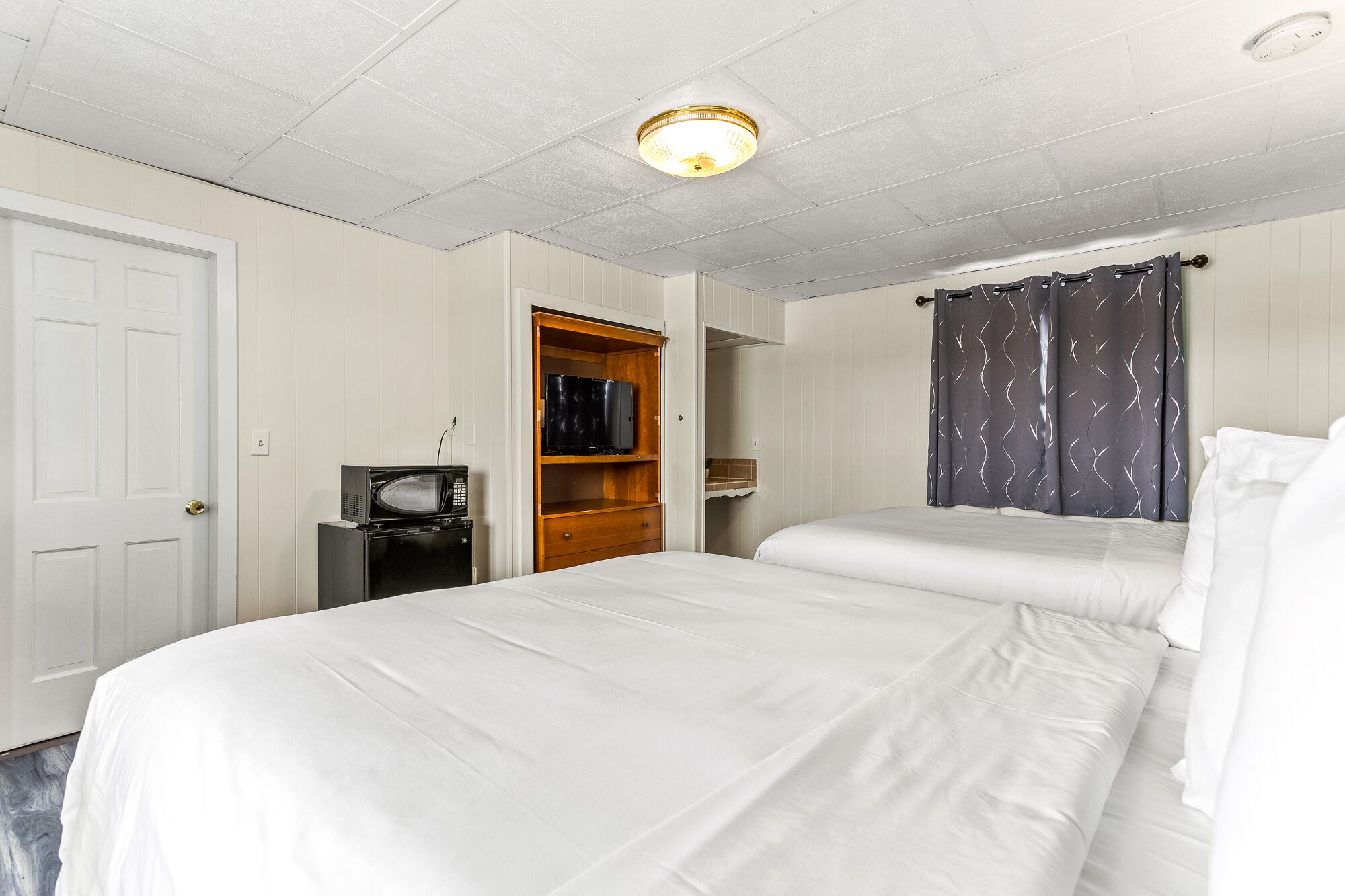 A hotel room with two beds, a wooden wardrobe, a microwave, and a television.