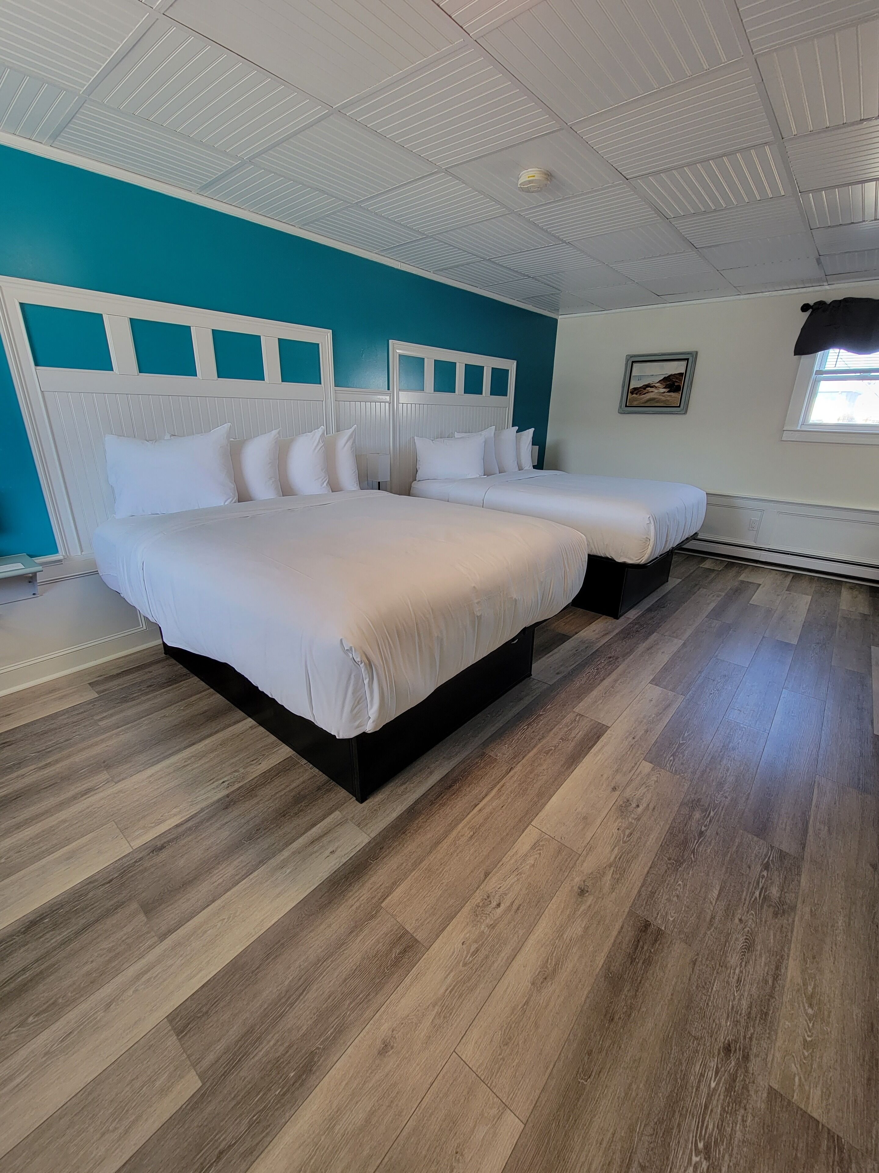 A bedroom with two beds, a white ceiling, and a teal wall.