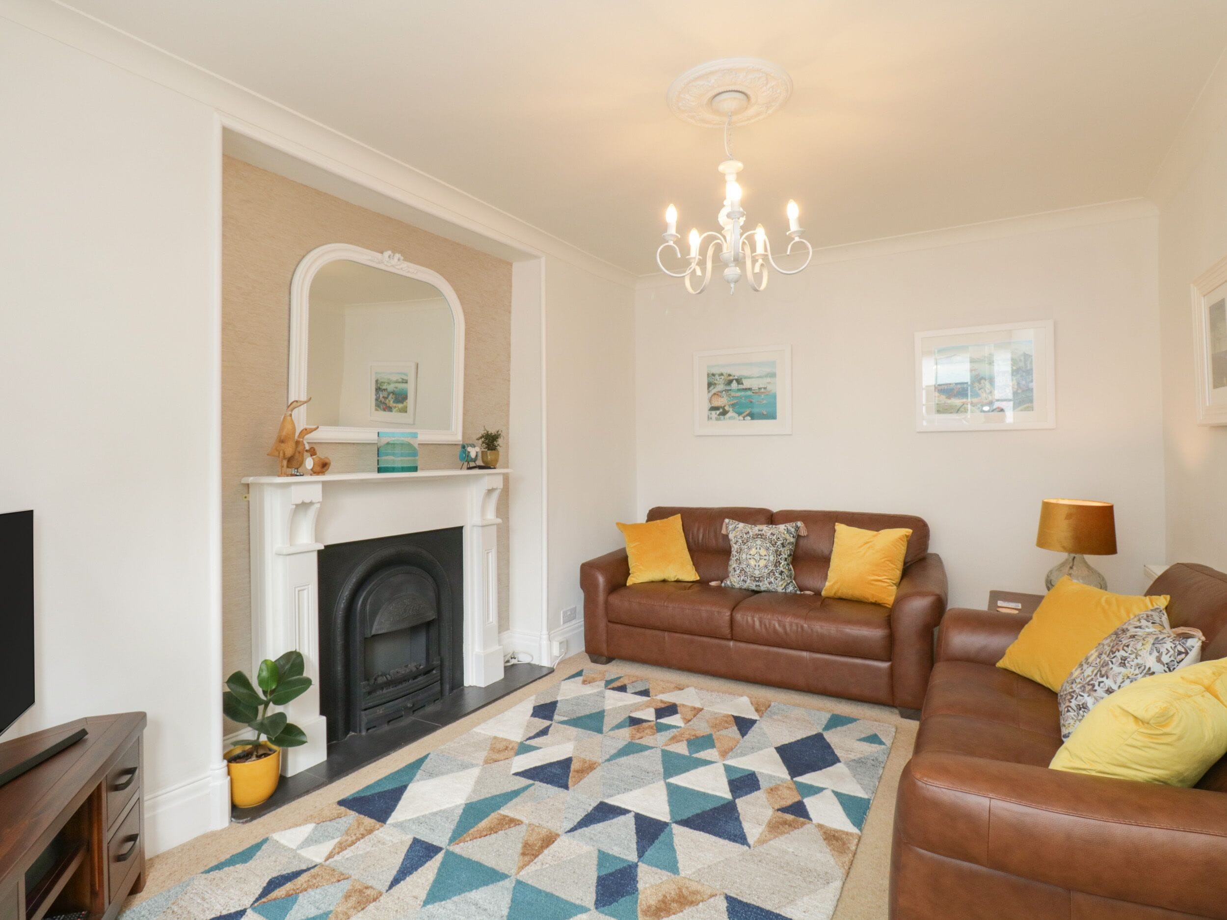 A living room with a fireplace, a brown leather sofa, a patterned rug, and a chandelier.