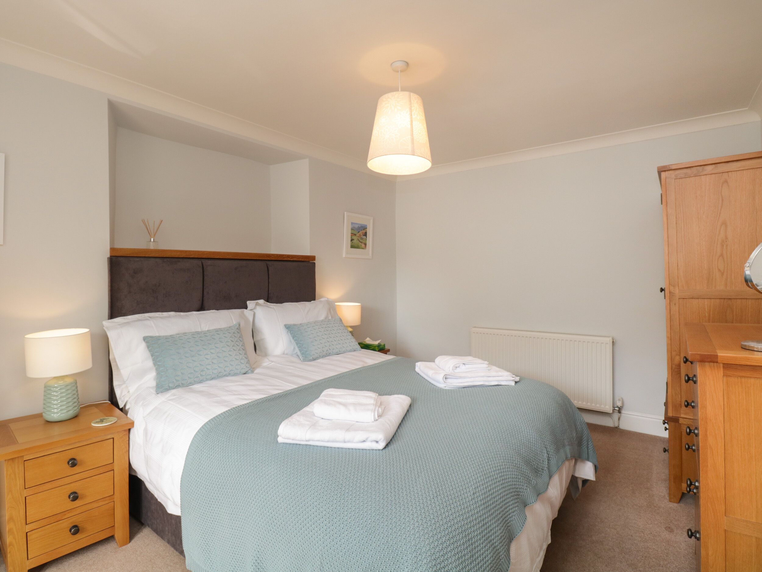 Une chambre bien rangée, avec un lit, des tables de chevet, une armoire et un luminaire suspendu.