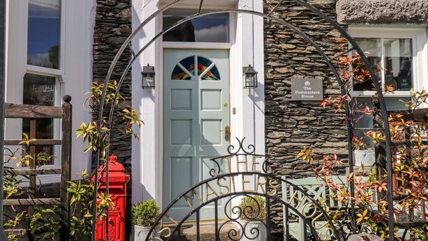A stone building with a white door, a red mailbox, and a sign that reads "The Postmasters House". - The Postmasters House (Windermere)