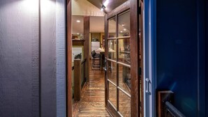 A hallway with a wooden door leading to a room with a kitchen area visible through the glass door. - Mountain Studio - luxury finishes in upscale neighborhood, e-bikes included! (Bozeman)
