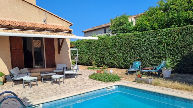 Una piscina con sillones de descanso y un patio cubierto.