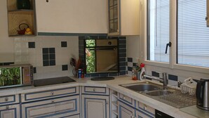 Una cocina con armarios blancos, horno empotrado, lavaplatos y una ventana con persianas.