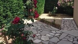 Un sendero de piedra que conduce a un jardín con rosales y una pérgola de madera.