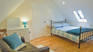 Une chambre avec un plafond en pente, un lit recouvert d’une couverture à carreaux, un bureau avec une lampe, une chaise et une fenêtre donnant sur un beau paysage.