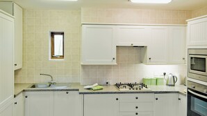 Une cuisine avec des meubles blancs, une cuisinière à gaz, un évier et une fenêtre.