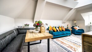 Un loft moderno con techo inclinado, una mesa de comedor de madera, un sofá, un diván azul y un tapete estampado.