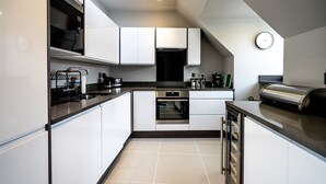 Una cocina moderna con armarios blancos, horno empotrado y cafetera.