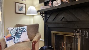 Una sala de estar acogedora con un sillón color beige, una chimenea negra y un estante con objetos decorativos.