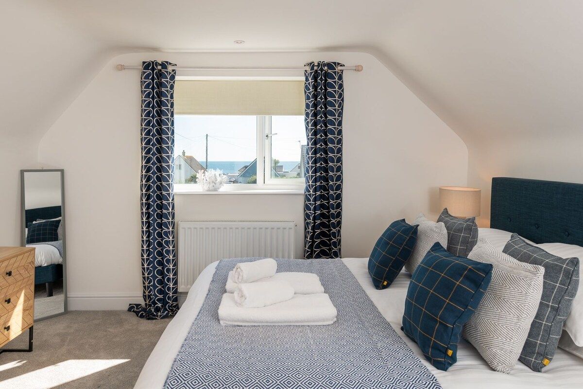 Une chambre à coucher avec un lit, des oreillers, une table de chevet, une lampe et une fenêtre avec des rideaux.