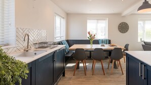 Een moderne keuken met een inbouwfornuis, een eethoek met een bank, en een grote klok aan de muur.