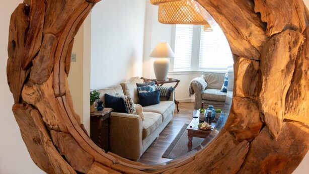 A living room with a round mirror, a sofa, a coffee table, and a lamp. - Bryn Awel Bach: 2-Bed Apartment in Central Rhosneigr | Managed by Anglesey Holiday Lettings (Rhosneigr)