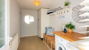 A laundry room with a washing machine, a drying rack, a mirror, and a welcome sign. - Bryn Awel Bach: 2-Bed Apartment in Central Rhosneigr | Managed by Anglesey Holiday Lettings (Rhosneigr)