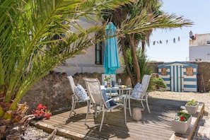 An outdoor patio with a table and chairs, a blue umbrella, and a small shed in the background. - Bryn Awel Bach: Two bedroom holiday apartment in Rhosneigr (Rhosneigr)