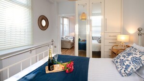 A bedroom with a bed, bedside table, lamp, and a mirror. - Bryn Awel Bach: 2-Bed Apartment in Central Rhosneigr | Managed by Anglesey Holiday Lettings (Rhosneigr)