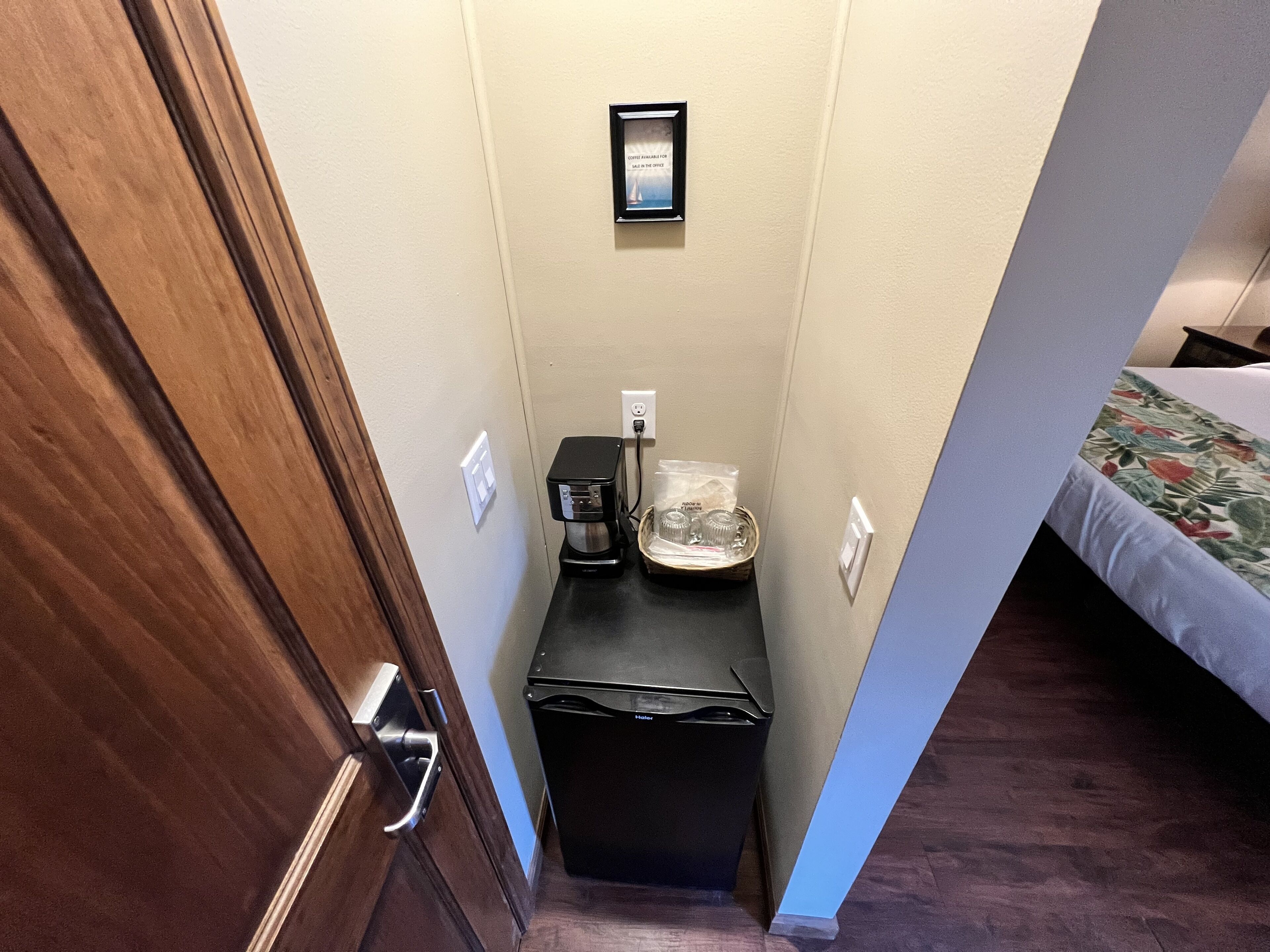 A narrow hallway with a coffee maker, a trash bin, and a framed sign on the wall.