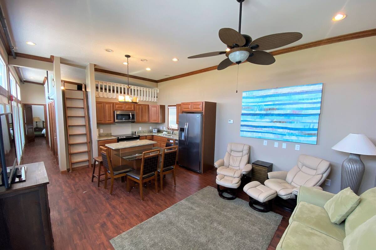 A spacious kitchen with wooden cabinets, a dining area with a table and chairs, a ceiling fan, and a large abstract painting on the wall.
