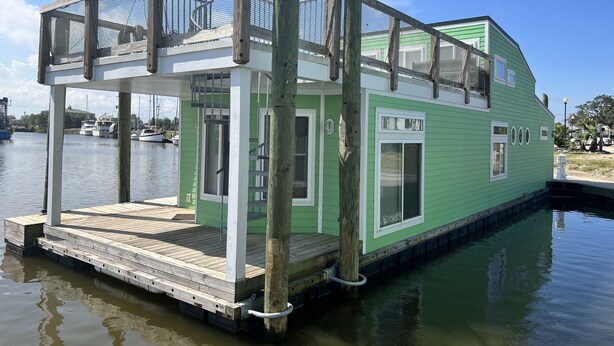 A green houseboat with a covered deck and a small staircase leading to the entrance. - New Orleans RV Resort & Marina (New Orleans)