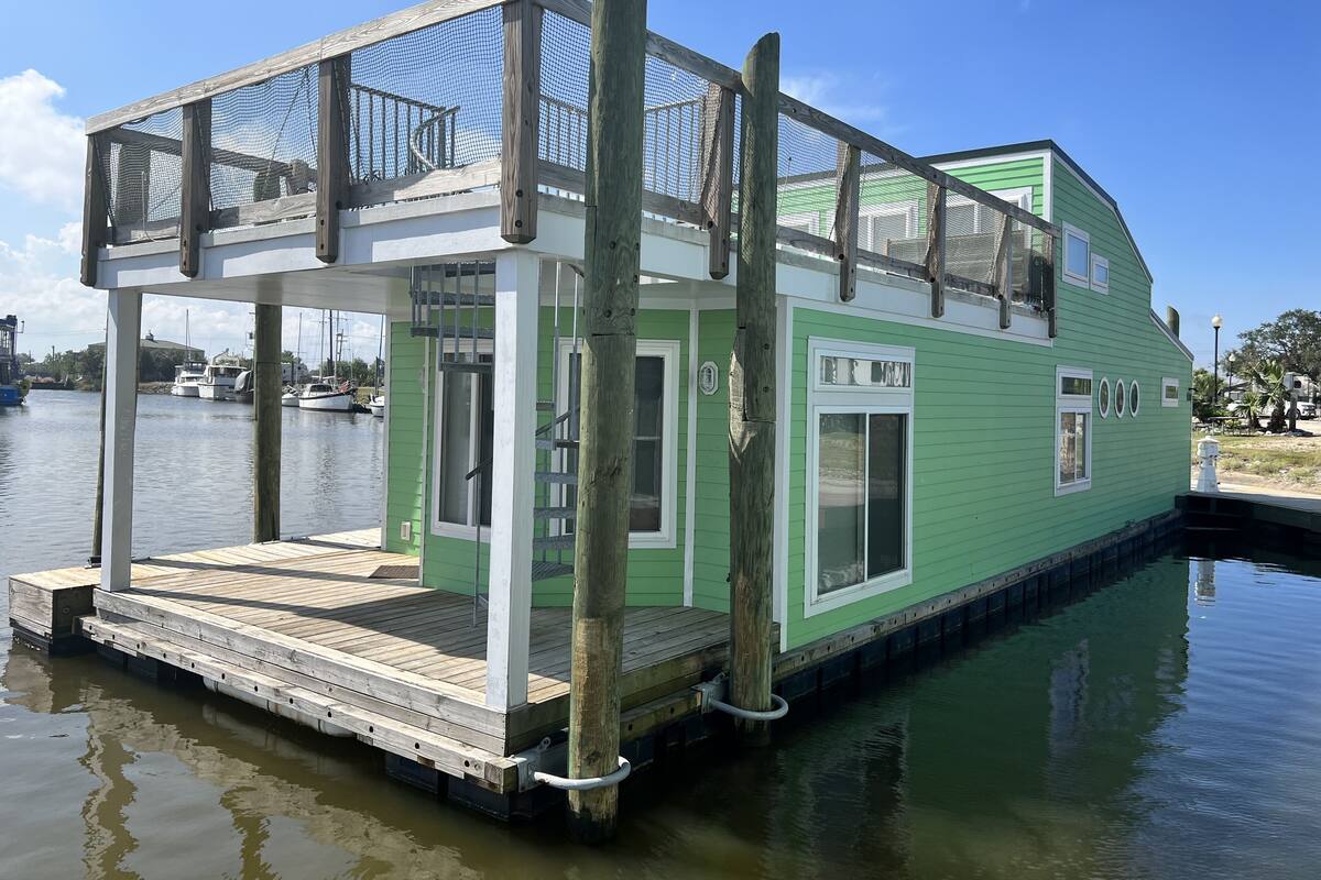 A green houseboat with a covered deck and a small staircase leading to the entrance.