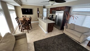 A modern kitchen with a central island, a dining area with wooden chairs, a flat-screen TV mounted on the wall, and a ceiling fan. - New Orleans RV Resort & Marina (New Orleans)