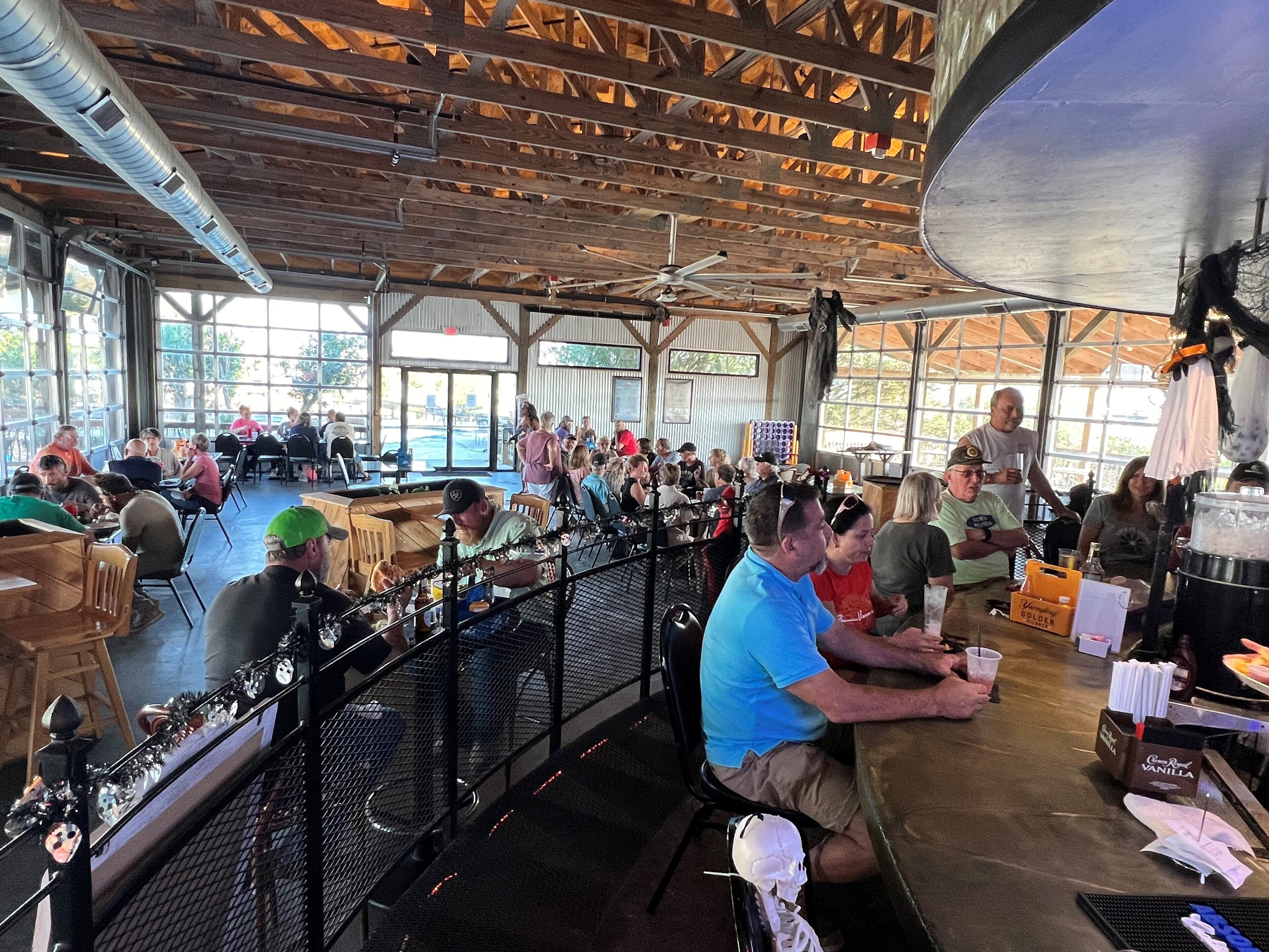 A spacious indoor venue with high ceilings and large windows, featuring tables and chairs arranged for dining or socializing.