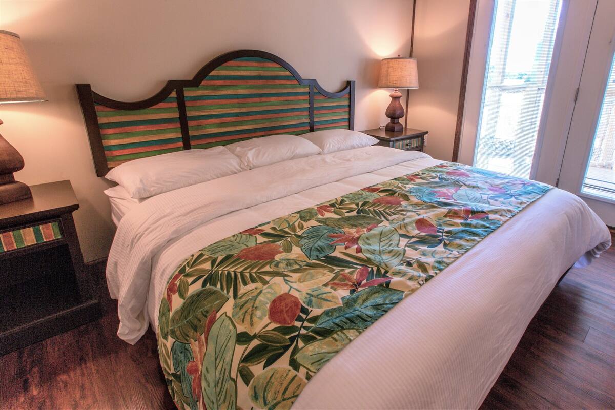 A neatly made bed with a floral bedspread, a wooden headboard with horizontal stripes, and two bedside lamps.