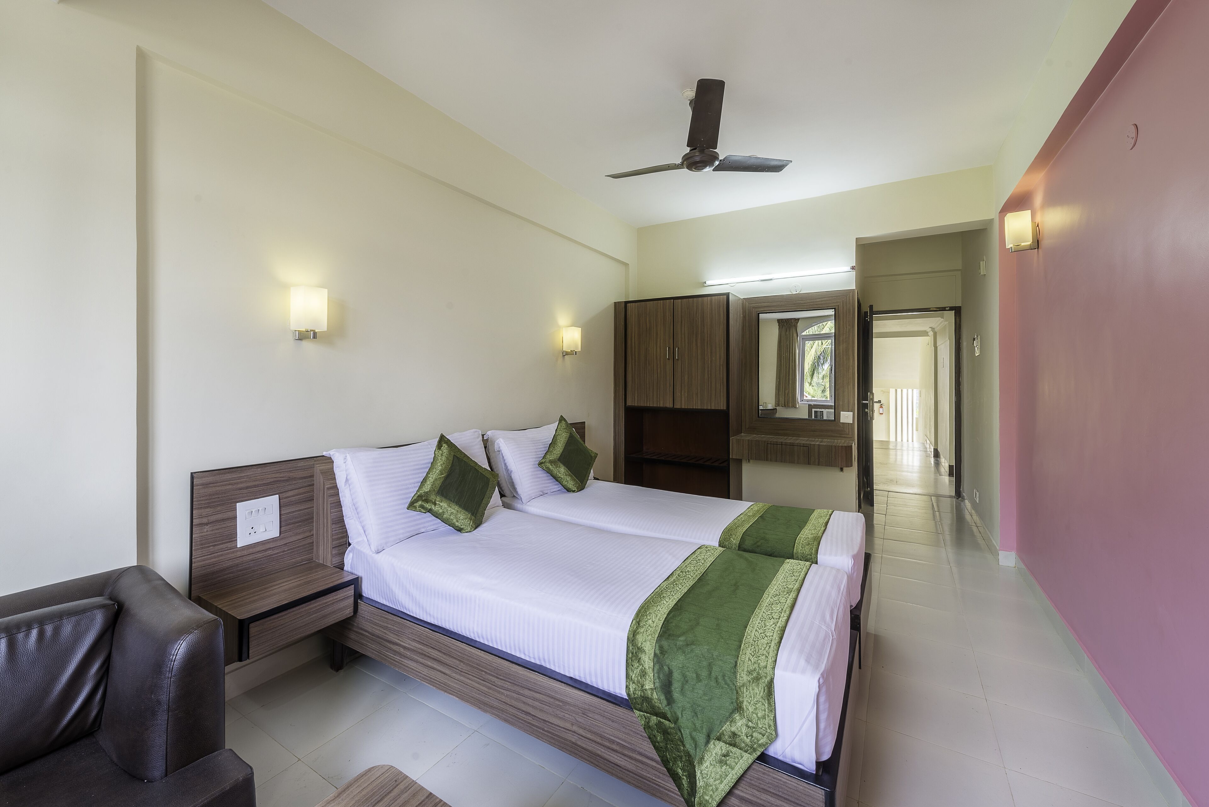 A hotel room with a large bed, a desk, a chair, and a ceiling fan.