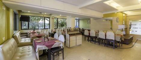 A spacious dining area with multiple tables and chairs, a sofa, and a kitchen counter.