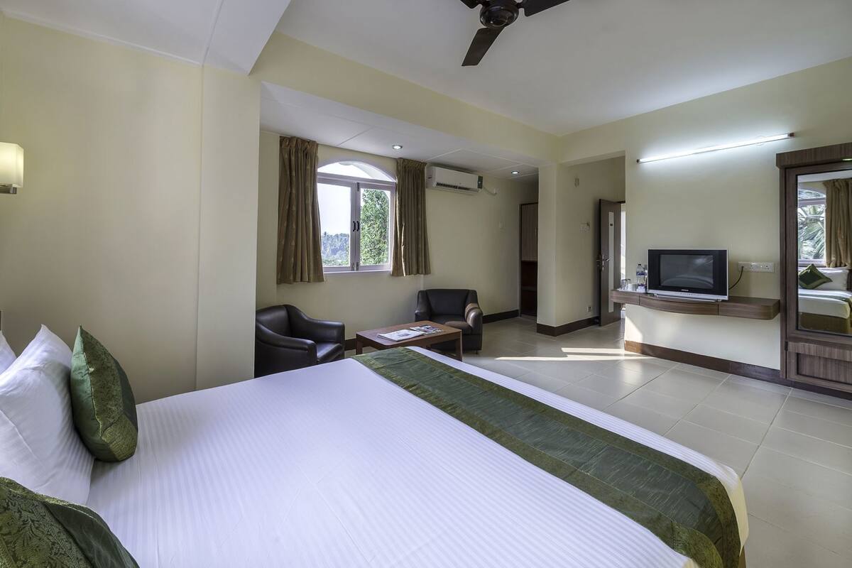 A hotel room with a bed, two chairs, a TV, and a ceiling fan.