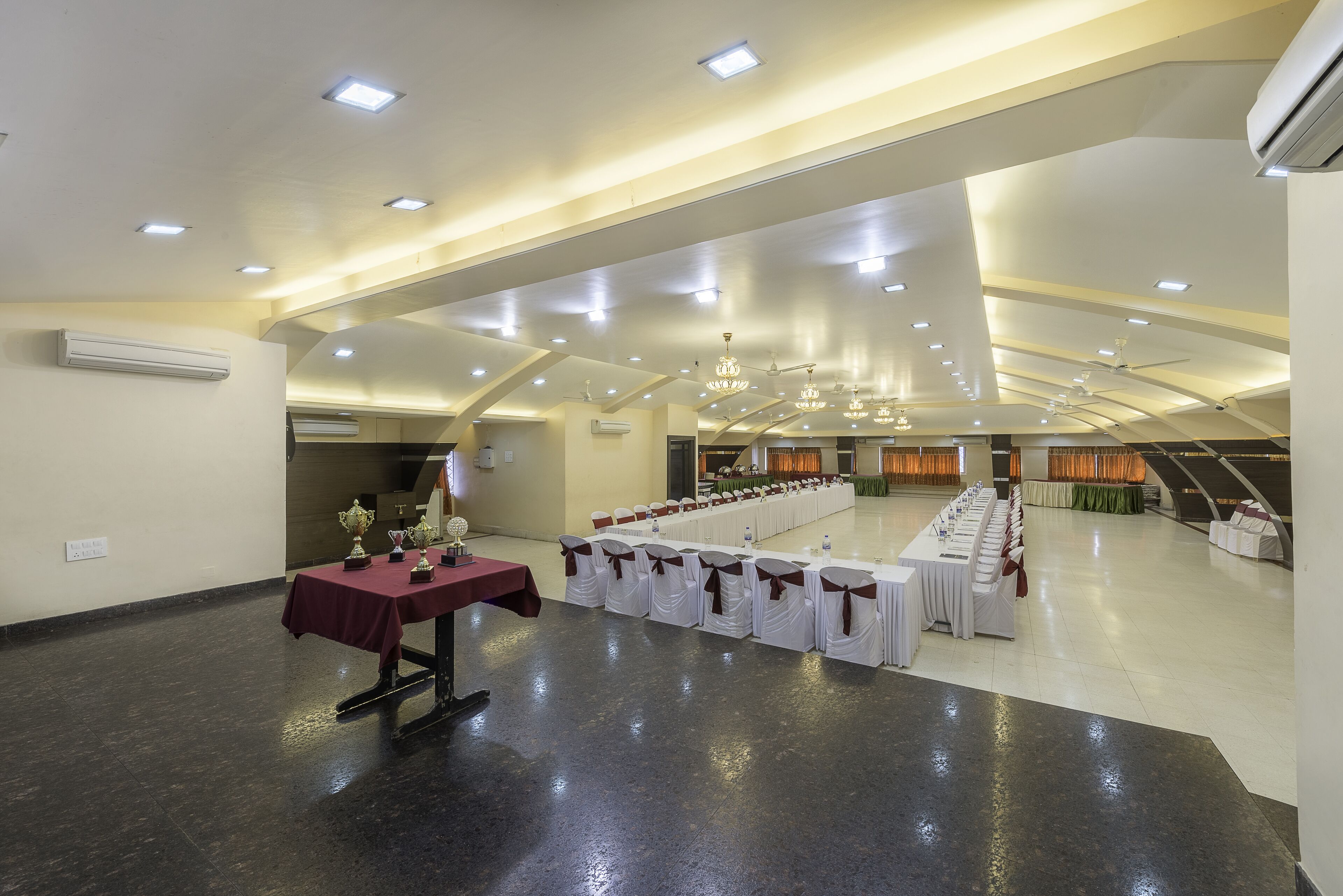 A spacious hall with a long table set for a banquet, white chairs with brown sashes, and a chandelier.