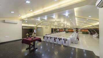 A spacious hall with a long table set for a banquet, white chairs with brown sashes, and a chandelier.